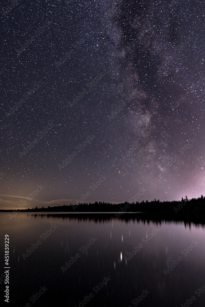 The Milky Way galaxy appears in the night sky over a calm lake.