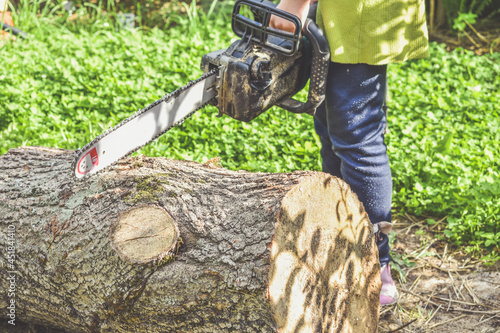 the girl child in a helmet with an electric saw saws a log