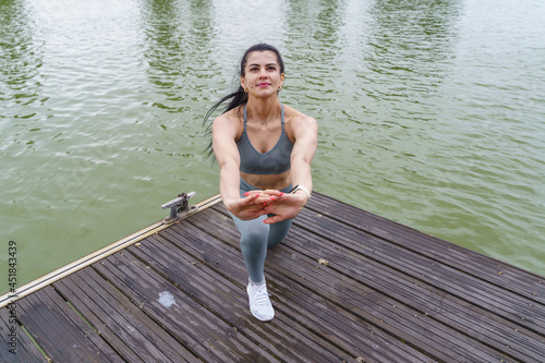 latin woman in sportswear stretching in river. Horizontal view of fitness woman training outdoors.