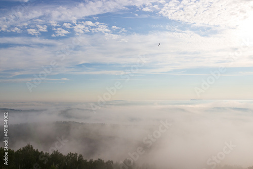 Summer landscape of early foggy morning over forest with cloudy sky. Heavy fog over horizon in Siberia  Russia