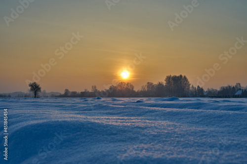 A snowy frozen field in the rays of the setting winter sun