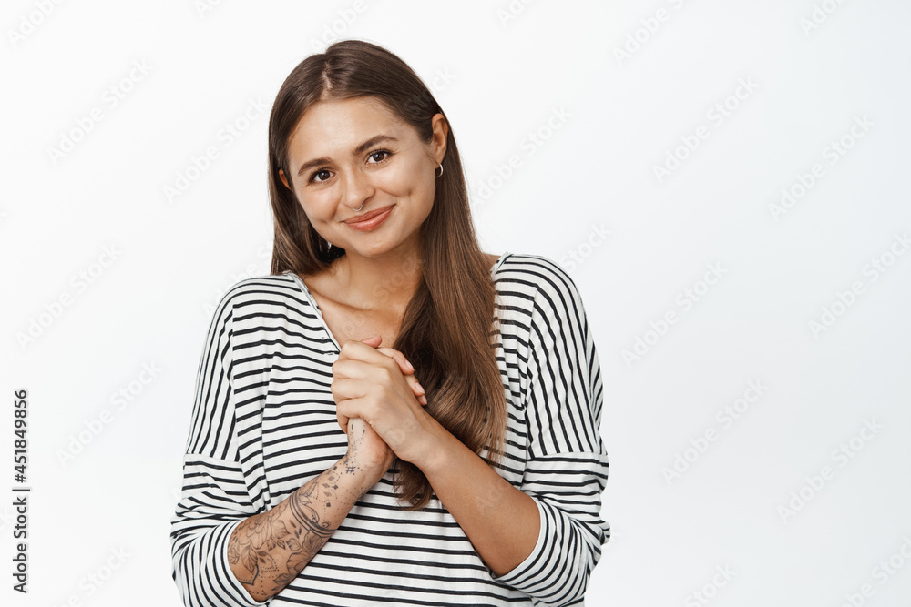 Image of cute girl holding hands clenched near chest and smiling flattered, showing thank you gesture, being grateful, standing over white background