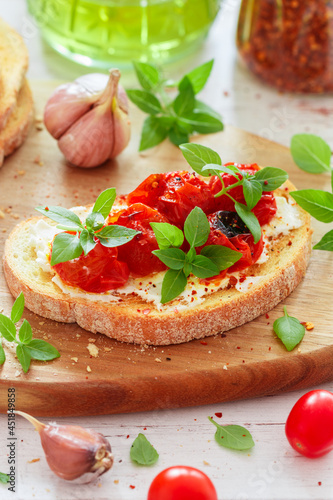 Bruschetta with baked cherry tomatoes, cream cheese (cottage cheese or ricotta), garlic, fresh basil and spices close-up. Mediterranean cuisine. A gourmet snack. Selective focus