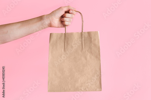 A man holds a craft package on a colored background. Blank space on a brown paper bag. Place for your text and logo. Copy space.