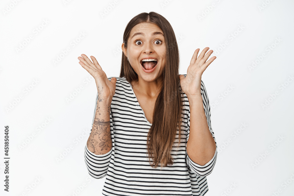 Image of surprised and happy woman reacts to big news, shaking hands near face and shouting from joy, white background Image of surprised and happy woman reacts to big news, shaking hands near face and shouting from joy, white background
