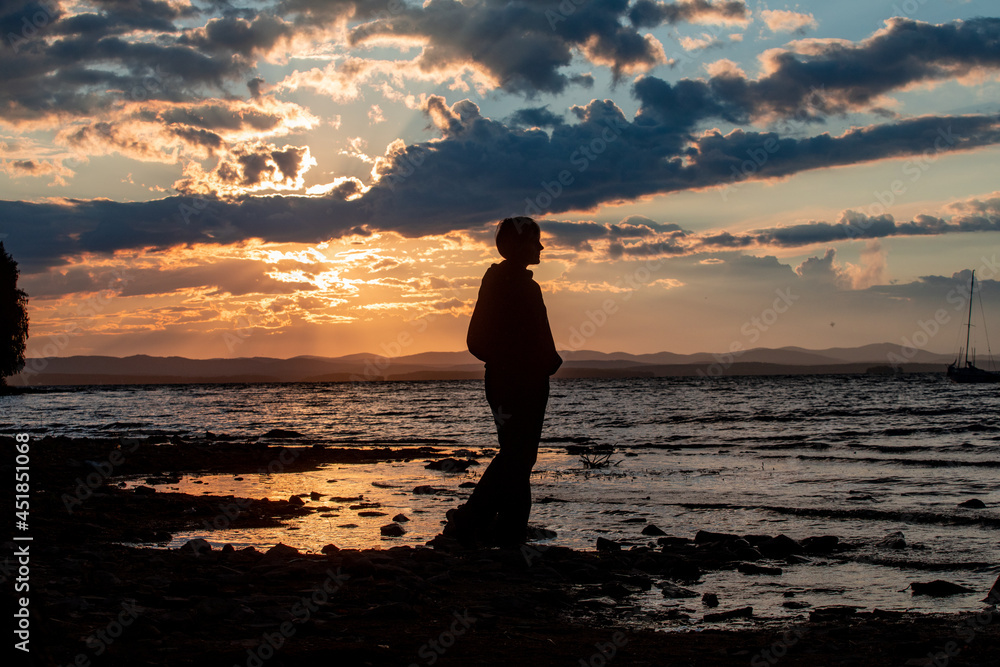 Mountain lake at sunset. The yacht sways on the waves. Silhouette of a girl at sunset Mountain lake at sunset. The yacht sways on the waves. Silhouette of a girl at sunset