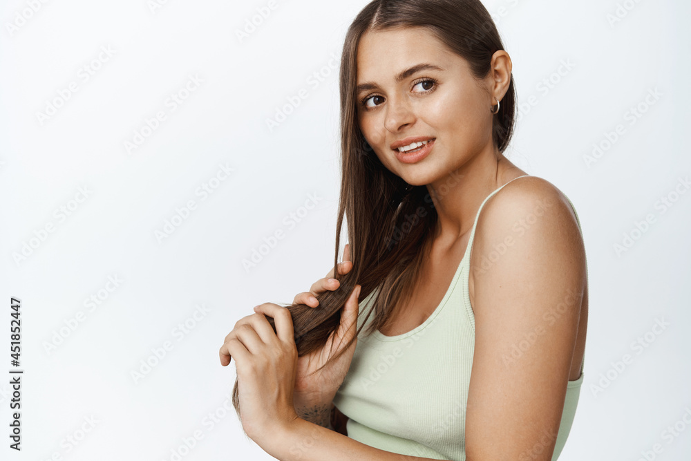 Portrait of young woman looking aside with sensual smile, combing her hair with hand, standing against white background Portrait of young woman looking aside with sensual smile, combing her hair with hand, standing against white background