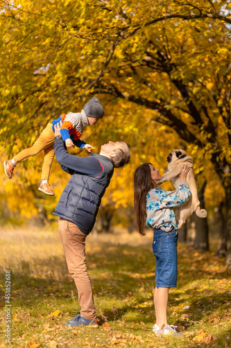 A young family with a small child and a dog spend time together for a walk in the autumn park
