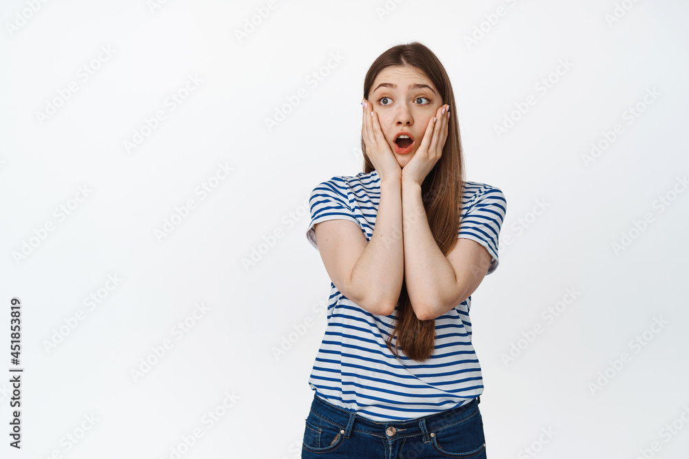 Impressed young woman drop jaw, gasping and looking left with shocked face expression, white background Impressed young woman drop jaw, gasping and looking left with shocked face expression, white background