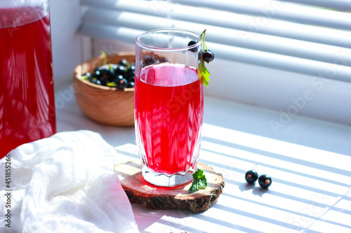 black currant juice with a glass glass on the window in the shade of the blinds, berries, summer soft drinks, healthy food