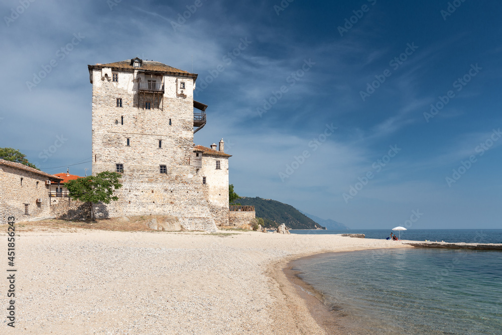 Big ancient Byzantine tower on an empty beach of a small Greek Mediterranean town against a blue sky with light clouds