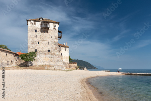 Big ancient Byzantine tower on an empty beach of a small Greek Mediterranean town against a blue sky with light clouds