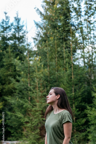 Young woman in forest. Portrait of a young caucasian girl in profile against background of trees, fir trees and forest. Relaxation meditation unity with nature