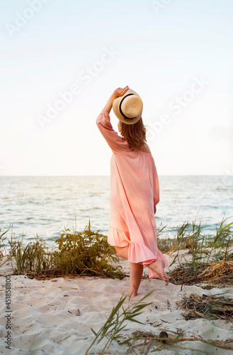 A beautiful young girl on the beach in a pink dress and a straw hat in her hands. Summer content, summer vacation. Energodar, Ukraine 19.08.2021 photo