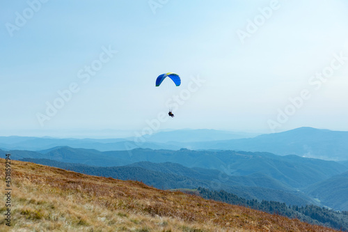 Paragliding over mountains with parachute. Paragliding behind blue sky hills range landscape. Active tourist sport People fly using Parachute.