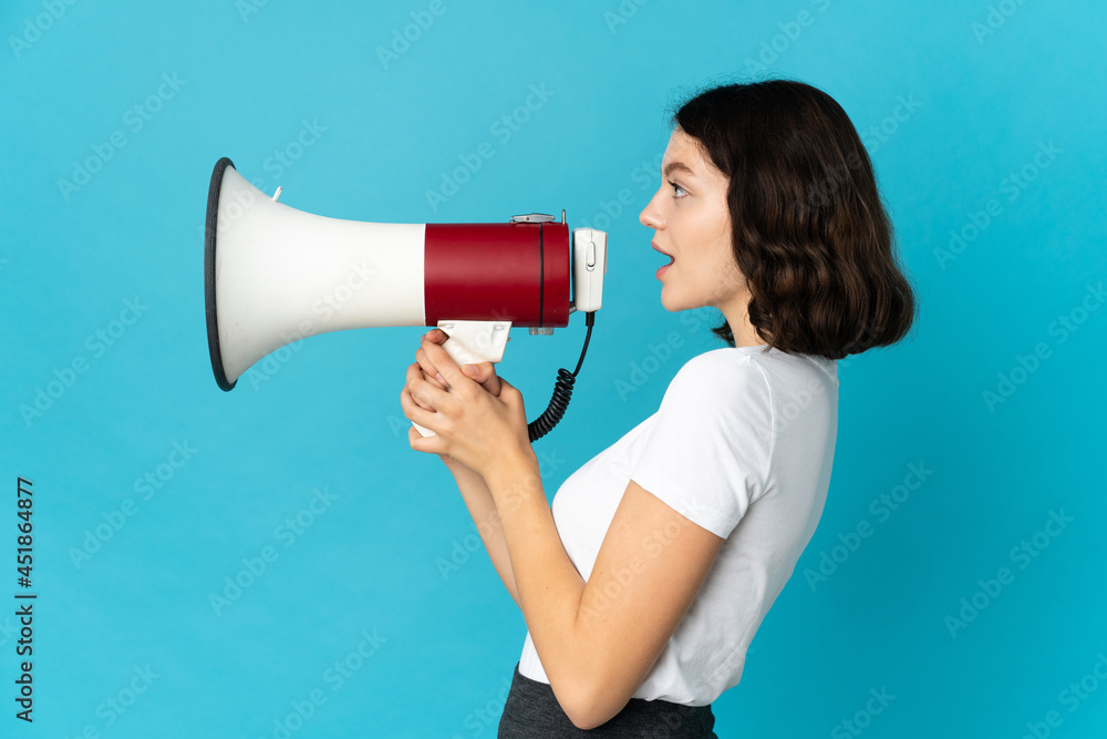 Teenager Ukrainian girl isolated on white background shouting through a megaphone to announce something in lateral position Teenager Ukrainian girl isolated on white background shouting through a megaphone to announce something in lateral position