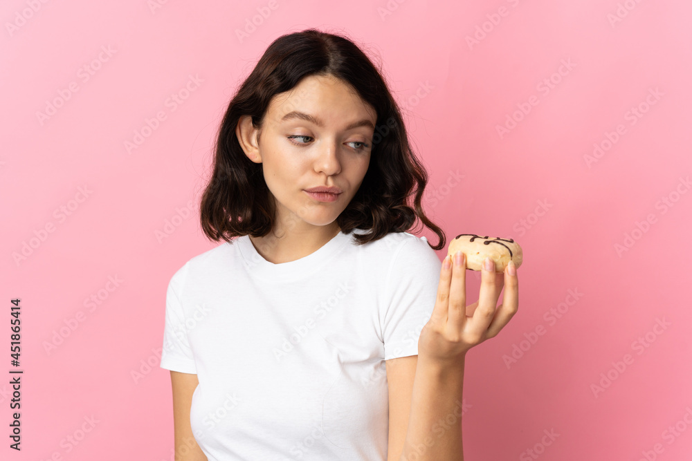 Teenager Ukrainian girl isolated on pink background holding a donut
