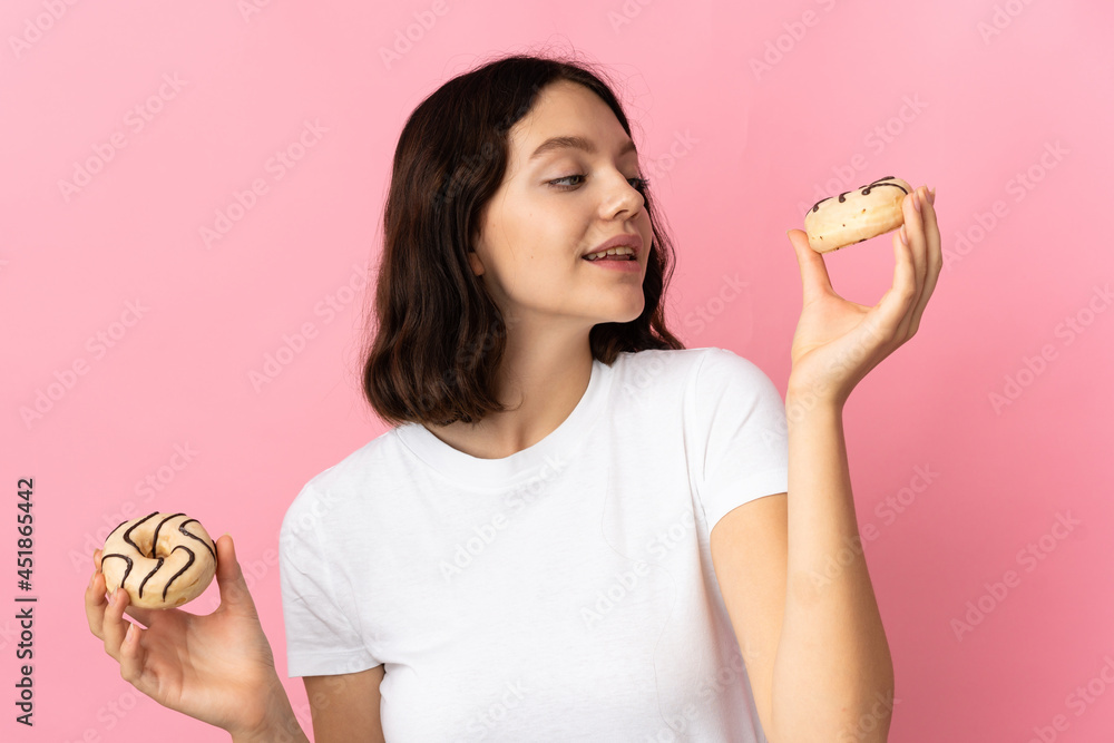 Teenager Ukrainian girl isolated on pink background holding donuts with happy expression Teenager Ukrainian girl isolated on pink background holding donuts with happy expression