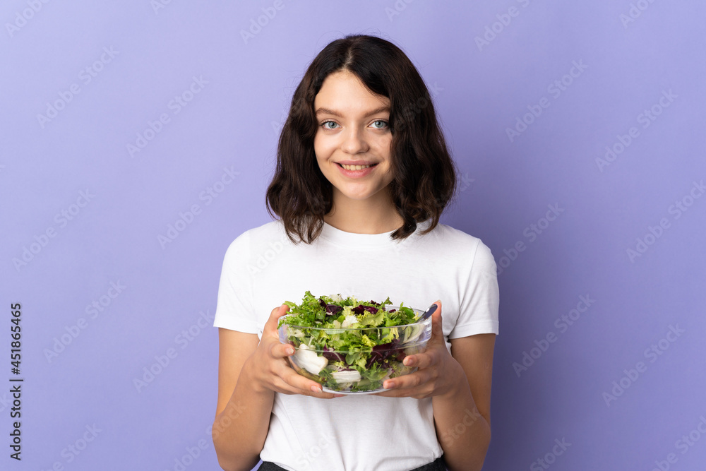 Teenager Ukrainian girl isolated on purple background holding a bowl of salad with happy expression