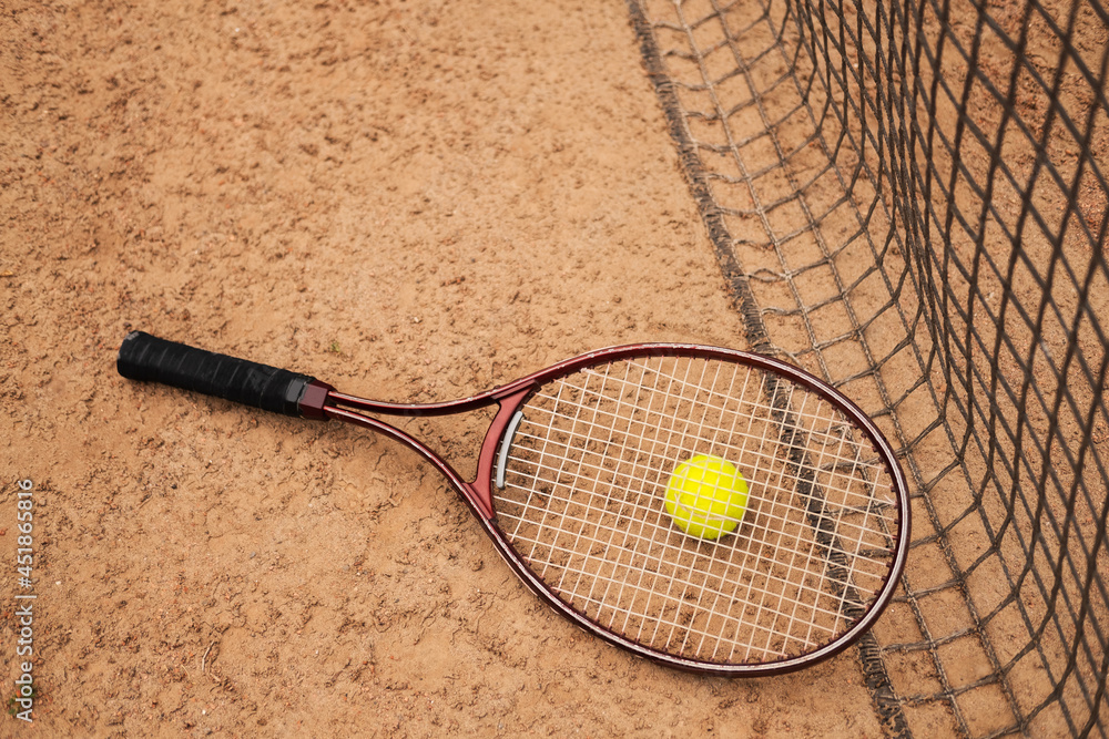 A bright yellow tennis ball and a tennis racket lie near the court net.