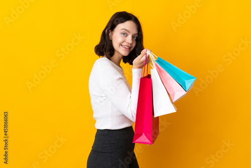 Teenager Ukrainian girl isolated on yellow background holding shopping bags and smiling