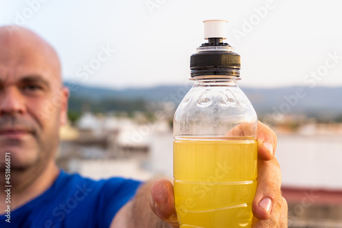 Принти на полотні Close-up of a plastic bottle with isotonic drink with a caucasian man in the background out of focus