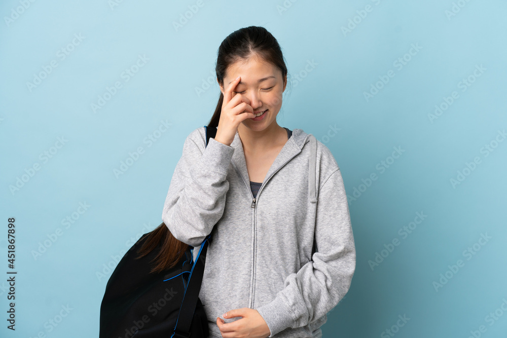 Young sport Chinese woman with sport bag over isolated blue background laughing Young sport Chinese woman with sport bag over isolated blue background laughing