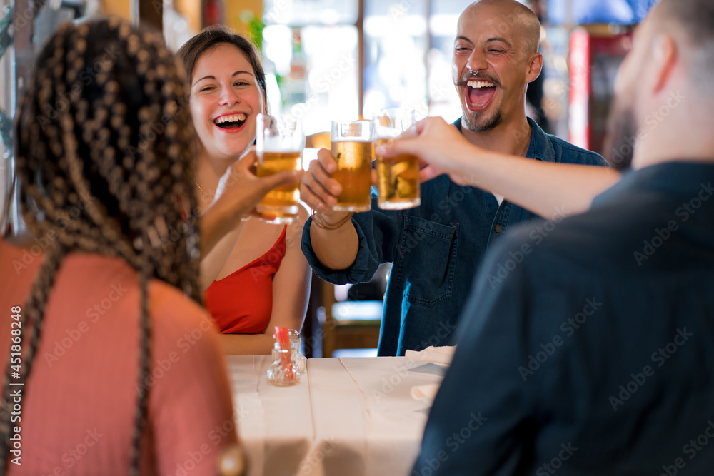 Group of friends toasting with beer glasses at a restaurant.