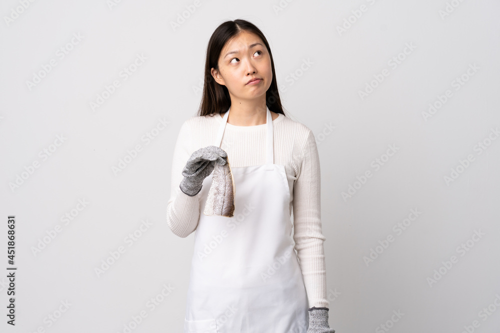 Chinese fishmonger wearing an apron and holding a raw fish over isolated white background and looking up Chinese fishmonger wearing an apron and holding a raw fish over isolated white background and looking up