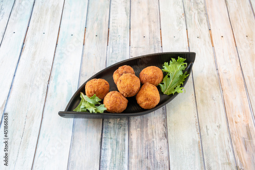 Black tray with round ham croquettes battered and fried in olive oil on wooden table
