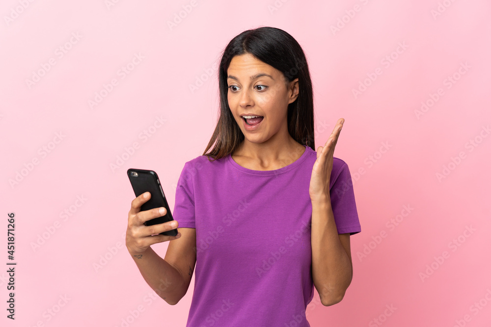 Caucasian girl isolated on pink background looking at the camera while using the mobile with surprised expression Caucasian girl isolated on pink background looking at the camera while using the mobile with surprised expression