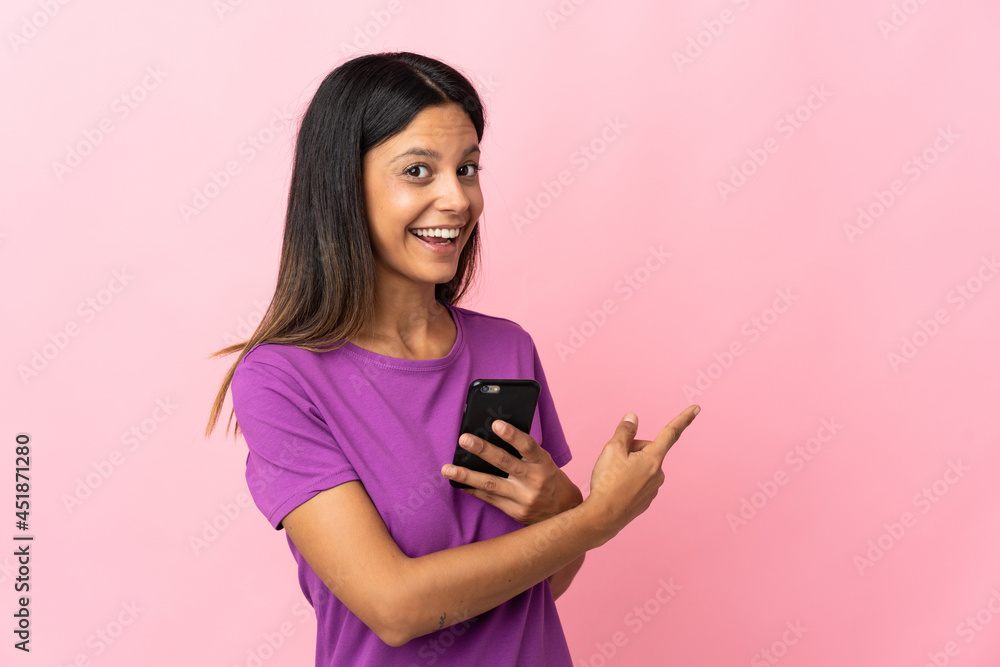 Caucasian girl isolated on pink background using mobile phone and pointing back Caucasian girl isolated on pink background using mobile phone and pointing back