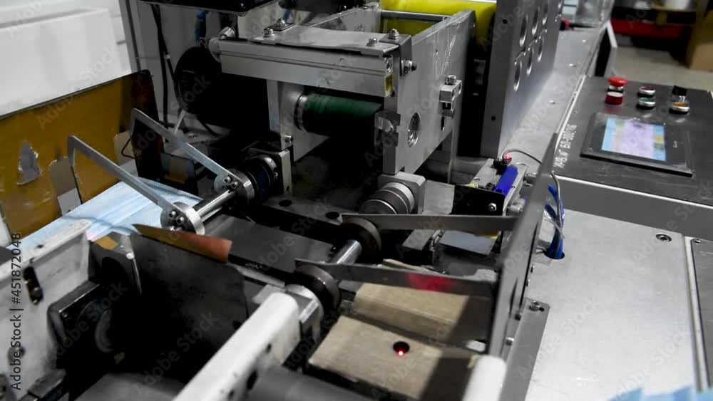 Production of medical three-layer blue or white masks. New masks move on a conveyor belt. Making protective masks during the coronavirus pandemic Production of medical three-layer blue or white masks. New masks move on a conveyor belt. Making protective masks during the coronavirus pandemic
