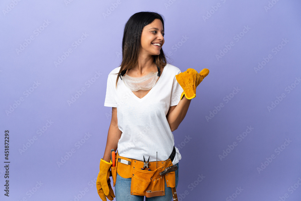 Young electrician woman isolated on purple background pointing to the side to present a product Young electrician woman isolated on purple background pointing to the side to present a product