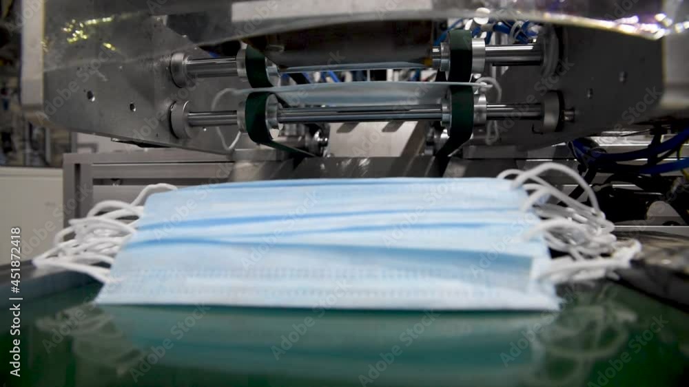 Production of medical three-layer blue or white masks. New masks move on a conveyor belt. Making protective masks during the coronavirus pandemic Production of medical three-layer blue or white masks. New masks move on a conveyor belt. Making protective masks during the coronavirus pandemic