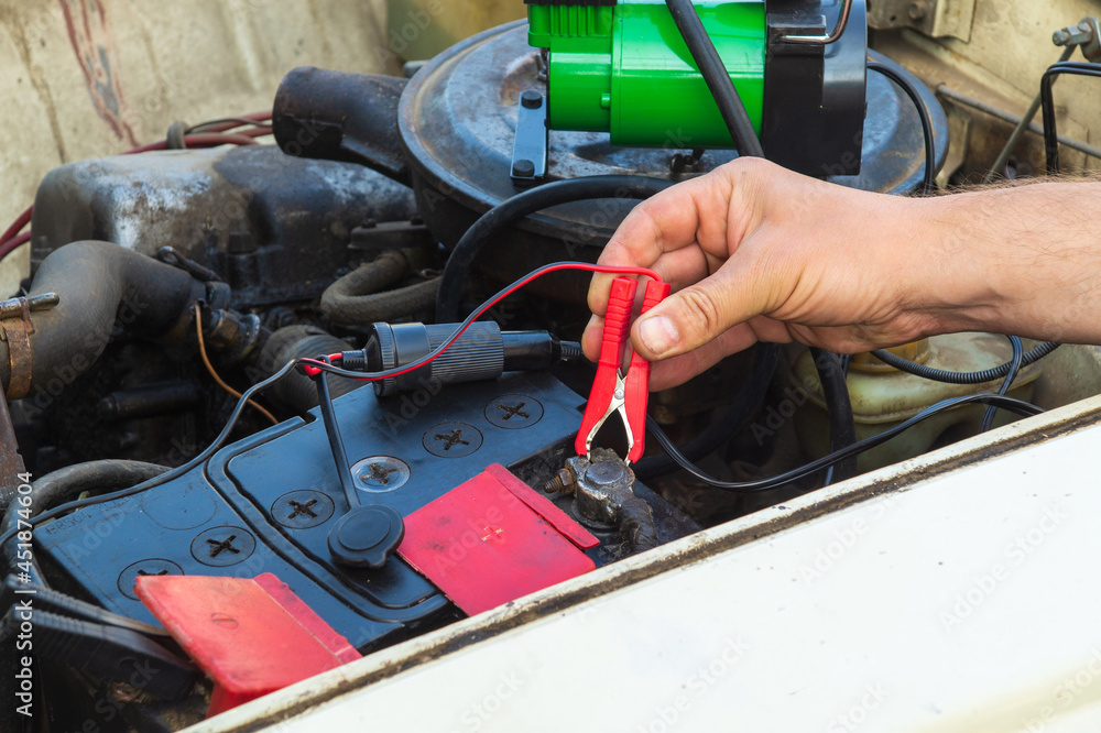 Close up of driver hand charging old car battery using electricity through jumper cables. Repair of an old car