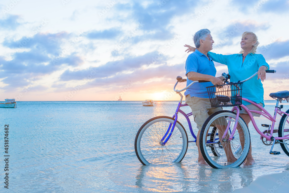 Happy senior couple exercising with bicycles on the beach on a sunset