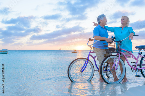 Happy senior couple exercising with bicycles on the beach on a sunset