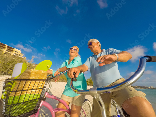 Happy senior couple exercising with bicycles on the beach on a sunny day © TRAVEL EASY