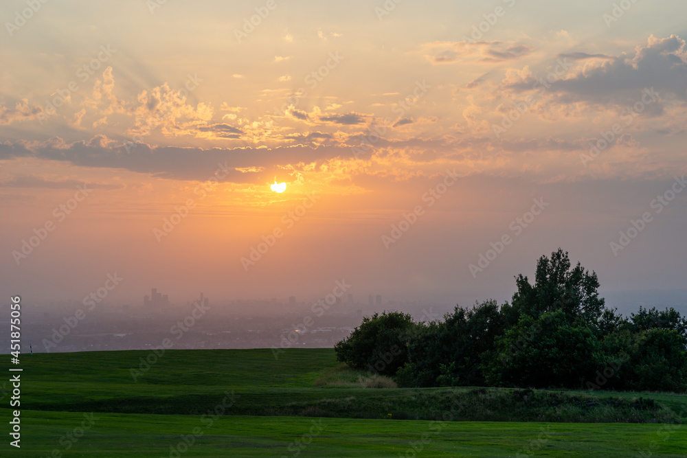 Sun setting over Manchester city on a dusty summer evening. The poor air quality and clouds helped produce a spectacular deep orange red sunset with sun rays. England, UK Sun setting over Manchester city on a dusty summer evening. The poor air quality and clouds helped produce a spectacular deep orange red sunset with sun rays. England, UK