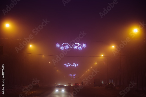 Night city lights above the city road. Traffic lights. Violet and yellow fog. Street Christmas garlands above the road.