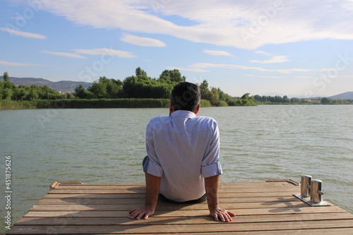 man sitting on the pier against the lake. man watching the lake on the dock