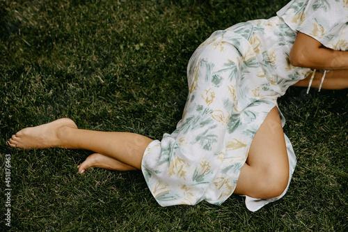 Barefoot woman, wearing a summer dress, lying on green grass, relaxing.