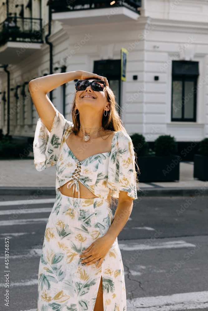 Beautiful young woman, wearing sunglasses and a summer dress, smiling, outdoors. Street fashion concept.