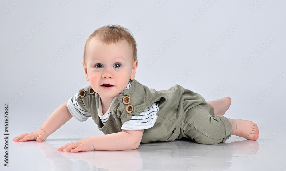 little boy in a green casual overalls, barefoot, lies on the floor and looks with interest into the frame. The kid stopped frozen crawling on the floor little boy in a green casual overalls, barefoot, lies on the floor and looks with interest into the frame. The kid stopped frozen crawling on the floor