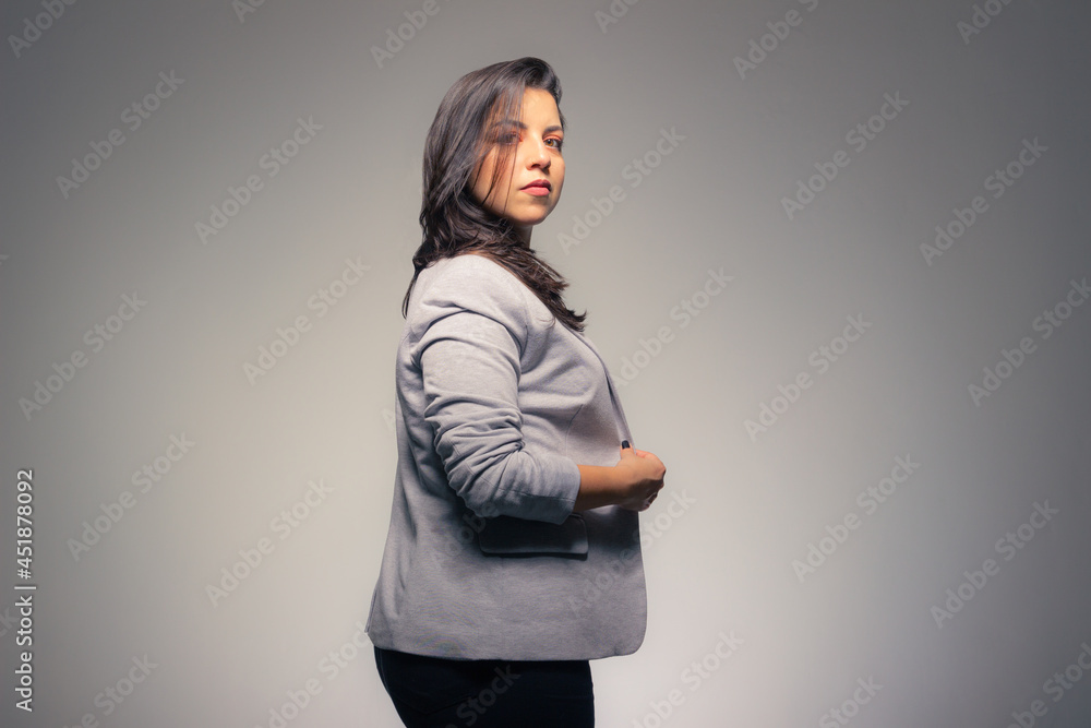 Charming business woman adjusting her clothes looking at camera with hair in her face on a gray background. Charming business woman adjusting her clothes looking at camera with hair in her face on a gray background.