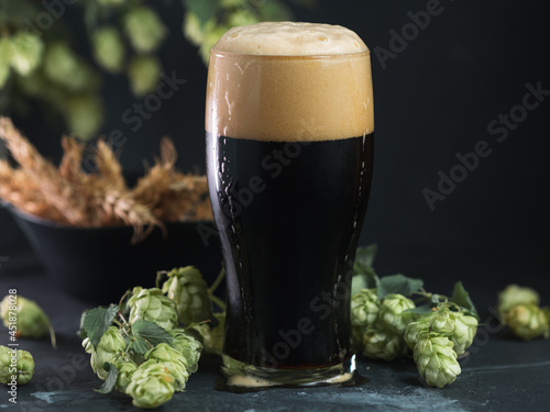 Fotografia glass of dark beer, craft stout or porter with green hop cones