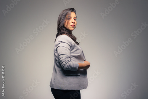 Charming business woman adjusting her clothes looking at camera with hair in her face on a gray background.