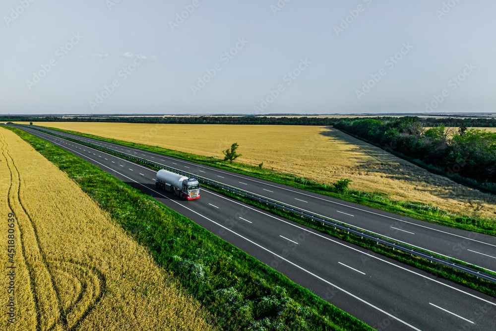 fuel truck on the higthway driving on asphalt road among the wheat fields. seen from the air. Aerial view landscape. drone photography. convoys with cargo