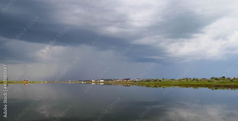 Estuary before a thunderstorm, a mirror image of the village, trees and dark thunderclouds